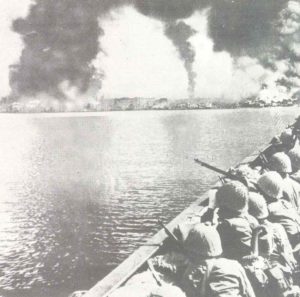 Japanese troops watch Manila burn from their landing craft. 